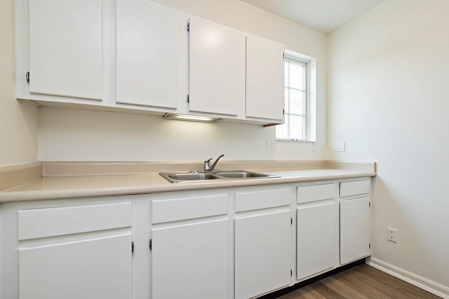 Plain white flat-panel stock cabinets with exposed hinges, a beige laminate counter and a stainless double sink.