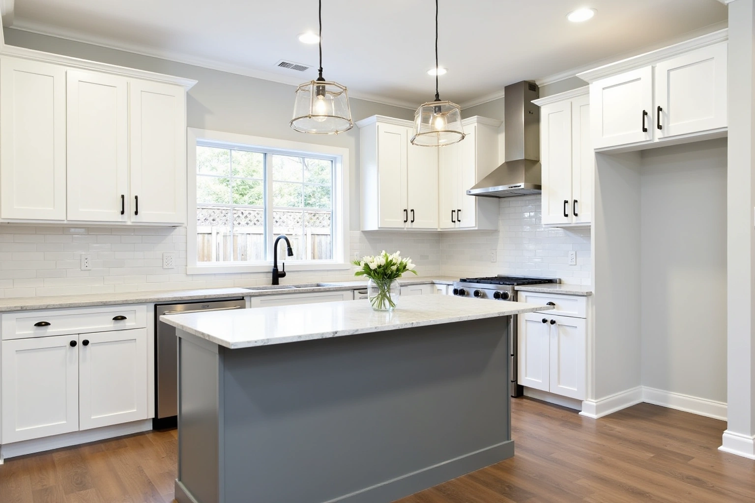 White shaker kitchen with matte black pulls, a grey island, white subway tile and two glass pendant lights.