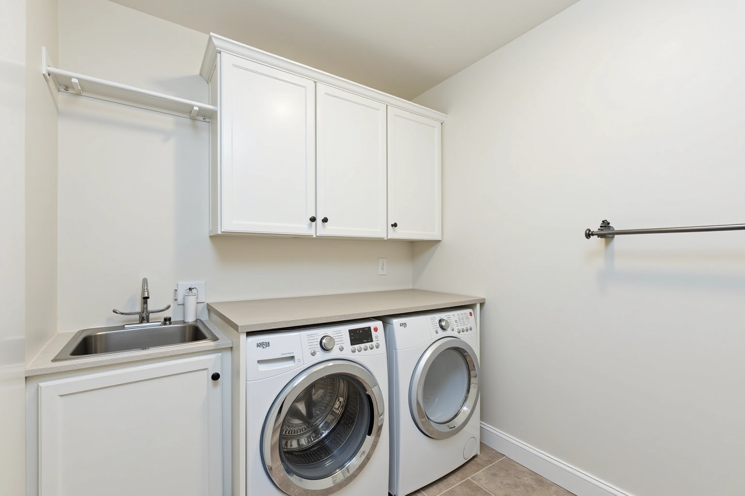 White upper cabinets over a front-load washer and dryer under a folding counter, with a utility sink and hanging rod.